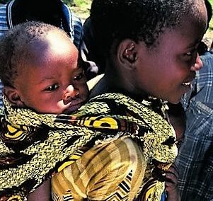 Ein Mädchen trägt sein Geschwisterchen in einem Kanga auf dem Rücken. (Quelle: Ralf Krämer)