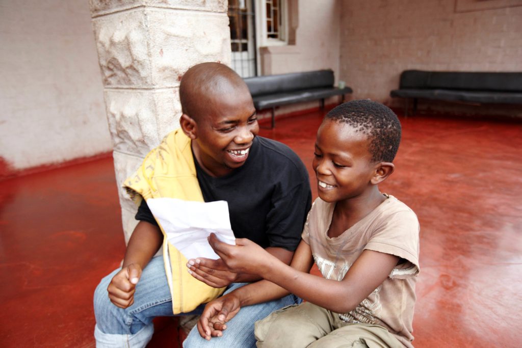 Ein Mitarbeiter in einem Straßenkinderprojekt in Südafrika übt mit einem Jungen Lesen. (Quelle: Frank Peterschröder)