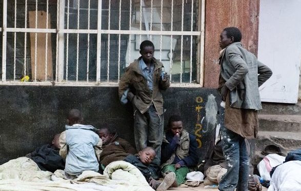 Straßenkinder liegen auf Pappe und Decken vor einem vergitterten Haus. (Quelle: Boland Brockmann)