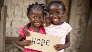 Zwei Mädchen halten ein Schild mit dem Wort "Hope" (Hoffnung) vor sich. (Quelle: iStock)