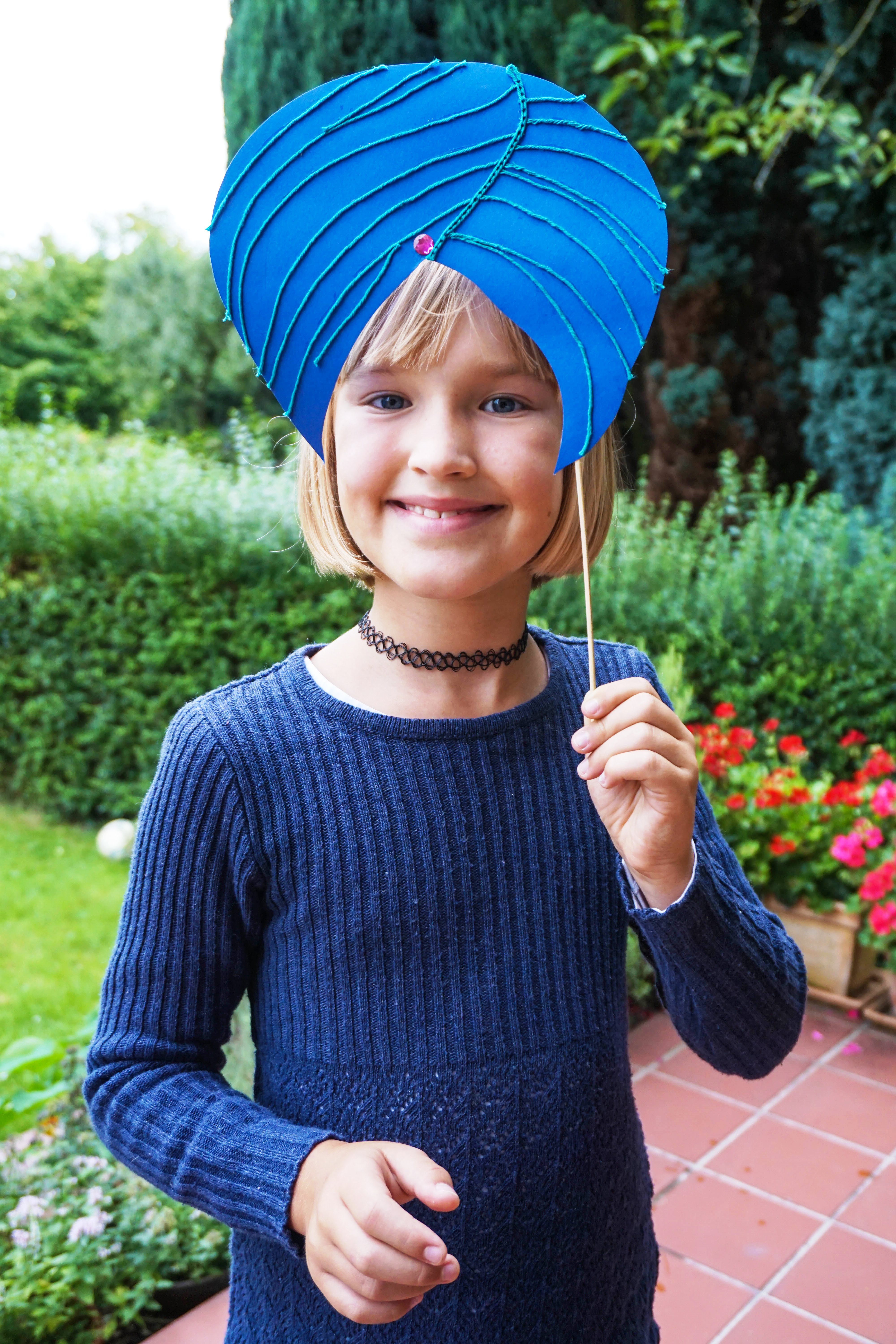 Ein Mädchen hält sich einen Turban aus blauem Tonpapier vor den Kopf. (Quelle: Ralf Krämer)