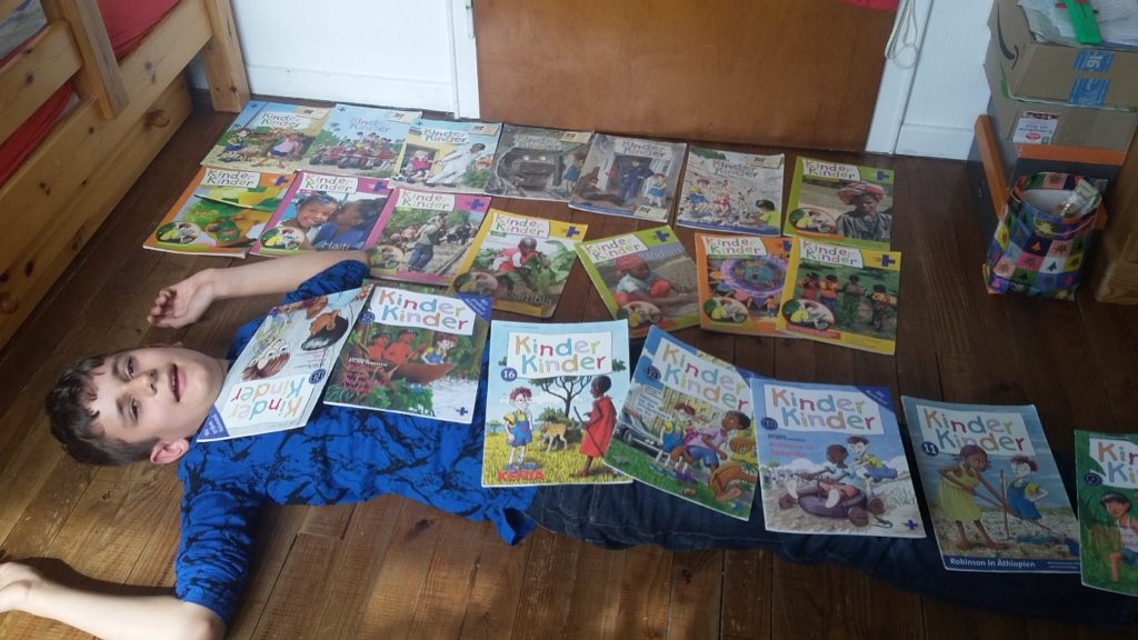 Ein Junge liegt auf dem Boden und hat sich mit "Kinder, Kinder"-Heften zugedeckt (Quelle: privat)