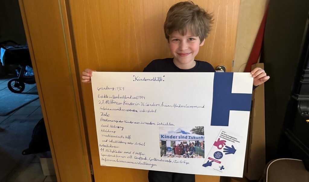 Ein Junge hält ein selbst gebasteltes Plakat mit Kindernothilfe-Logo hoch (Quelle: privat)