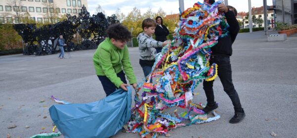 Kinder ziehen einen Wust aus bunten Papierschlangen aus einem Müllsack (Quelle: klein)